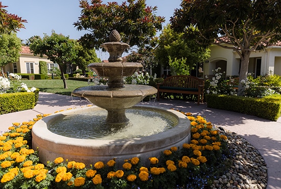 A fountain surrounded by flowers in a courtyard at La Costa Glen