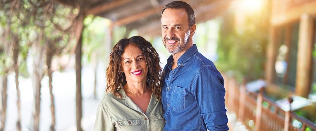 A smiling man and woman under a pergola embracing each other.